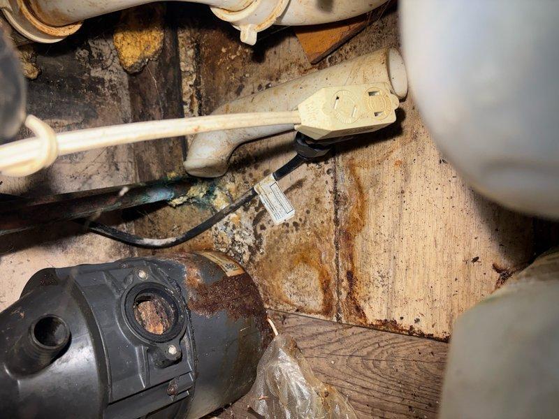 Responded to clogged sink service call and performed diagnostic inspection of drainage system. Upon arrival, accessed underside plumbing assembly in confined utility space to identify blockage source. Inspected P-trap, drain lines, and associated PVC fittings for obstruction or damage. Noted evidence of moisture exposure and previous water damage in surrounding wooden structural elements, indicating potential past overflow or leak issues. Examined electrical components and pump housing in vicinity, observing signs of corrosion that may require future attention. Cleared blockage from drain line to restore proper water flow and drainage function. Verified all connections secure and tested system operation to confirm resolution. Sink now draining properly with no backup or slow drainage issues.