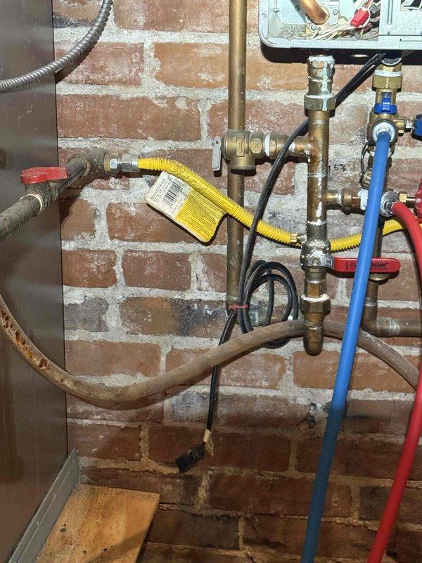 Responded to no hot water complaint on second floor. Upon arrival, inspected tankless water heater installation and associated plumbing connections mounted against brick wall. Evaluated gas supply line with yellow flexible connector, water supply lines with isolation valves (blue and red handles), and electrical connections. Diagnosed issue with water flow or gas supply affecting unit operation. Verified proper valve positions, checked brass ball valve and compression fittings for functionality, and ensured gas line connections were secure per manufacturer specifications. Restored hot water service to second floor. System tested and confirmed operational upon completion.