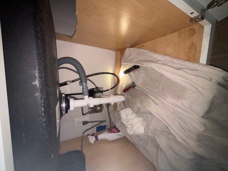 Performed camera inspection of residential plumbing system in utility cabinet space. Documented existing PVC drain assembly configuration, including white PVC piping with flexible hosing connections and blue-handled shutoff valve, noting wall staining and discoloration that may indicate previous moisture issues or drainage concerns.