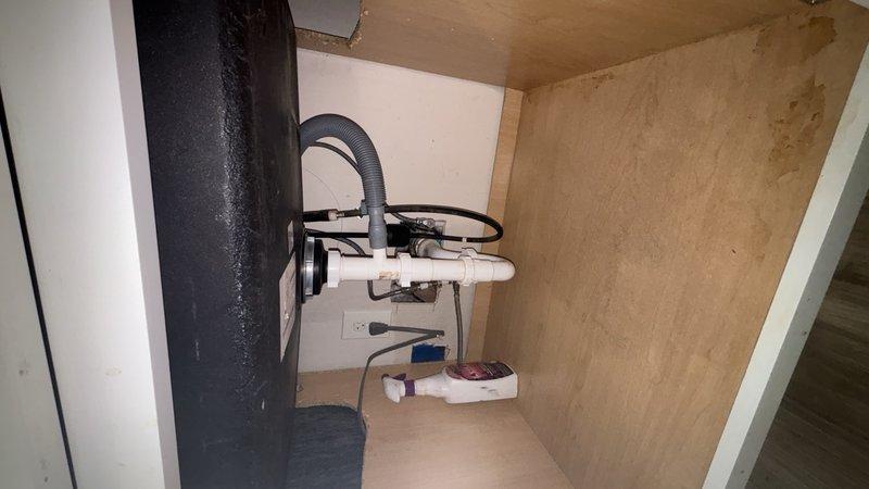 Performed camera inspection of residential plumbing system in utility cabinet space. Documented existing PVC drain assembly configuration, including white PVC piping with flexible hosing connections and blue-handled shutoff valve, noting wall staining and discoloration that may indicate previous moisture issues or drainage concerns.
