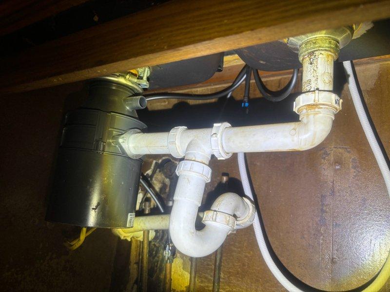 Responded to reported leaking faucet in kitchen. Upon inspection, identified worn supply line connections and deteriorated shut-off valve causing water seepage beneath sink. Accessed under-sink plumbing assembly featuring garbage disposal unit connected to PVC P-trap drainage system. Inspected brass tailpiece connections showing mineral buildup and corrosion contributing to leak issue. Tightened supply line fittings and assessed valve condition. Examined main water supply lines in mechanical space, noting aged copper piping with surface oxidation and compromised foam insulation, though structural integrity remained intact. Verified proper drainage flow through P-trap assembly and confirmed all connections secured with appropriate clamps. Leak successfully resolved and system restored to proper working condition.
