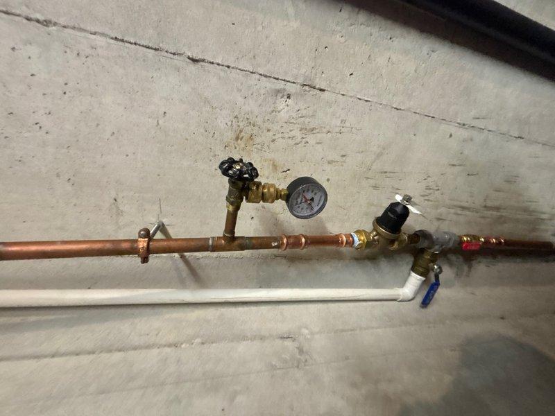 Installed customer-supplied pressure reducing valve (PRV) on main water line with brass fittings and shut-off valves. System tested and verified proper operation with pressure gauge reading approximately 90 PSI, ensuring adequate water pressure regulation for the property.