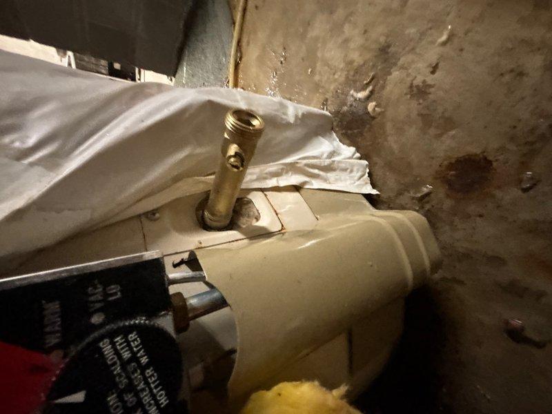 Responded to water heater leak in basement utility area. Upon arrival, found significant water pooling on concrete floor with visible staining and moisture damage throughout the space. Inspected water heater and identified leak originating from temperature and pressure relief valve assembly. The brass valve fitting showed signs of failure, causing active water discharge onto the floor. Assessed surrounding insulation and protective covering for water damage. Documented conditions with photographs showing extent of water accumulation and compromised valve component. Provided customer with findings and recommendations for relief valve replacement to resolve the active leak and prevent further water damage to the basement floor and surrounding area.