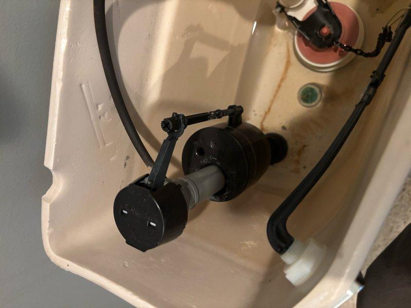 Responded to service call for three leaking toilets located on two levels of the residence. Inspected toilet tank components in primary bedroom on main level, identifying worn flush valve assembly and deteriorated fill valve mechanisms as sources of water leakage. Tank interior showed mineral deposits and rust-colored staining indicating age-related wear and potential seal degradation. Examined internal plumbing connections, including flush valve with cylindrical body, connecting tubes, and rubber overflow hose, as well as fill valve with float assembly and water supply connections. Documented condition of all internal mechanical components and their arrangement within tank for repair assessment.