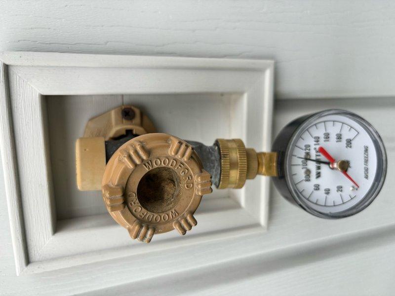 Completed comprehensive whole-home plumbing inspection per customer request from promotional campaign. Thoroughly evaluated water heater installation in utility closet, including copper supply lines, blue corrugated discharge piping, and associated components such as expansion tank or filtration system mounted to overhead plumbing. Inspected WOODFORD brand pressure regulator valve assembly installed in recessed wall box with accompanying pressure gauge to verify proper system pressure regulation and monitoring capability. Documented all findings with photographic evidence for customer records.
