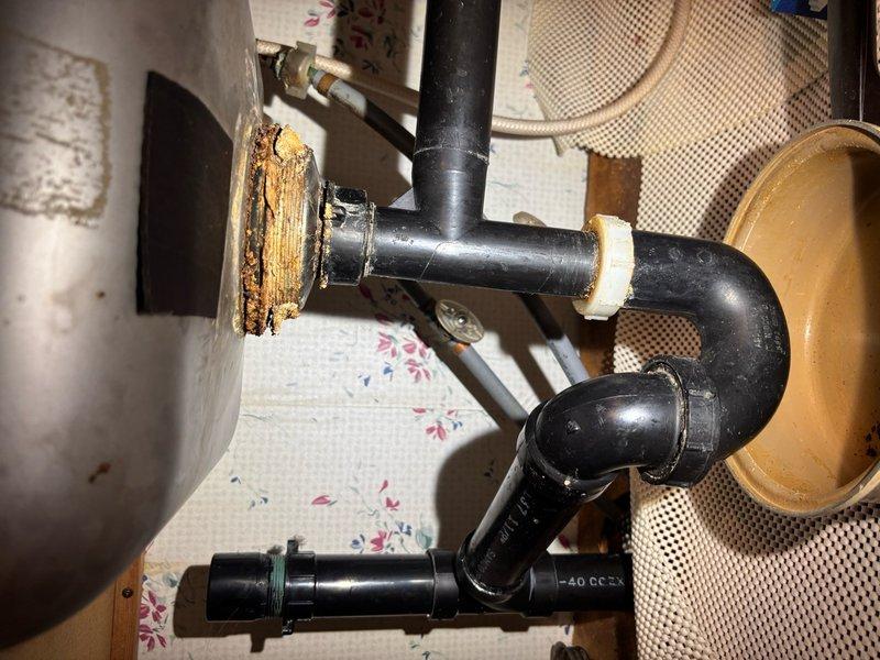 Responded to clogged kitchen sink complaint and performed diagnostic inspection of drainage system. Upon investigation, discovered significant corrosion and deterioration at wall connection point of drain piping, with extensive rust buildup indicating long-term water damage and potential leak source. Documented existing P-trap configuration with black ABS piping and identified compromised pipe connection as contributing factor to drainage issues. Photographed corroded wall fitting and surrounding plumbing components for repair recommendations. Additional repairs required to address deteriorated pipe connection and restore proper drainage function.