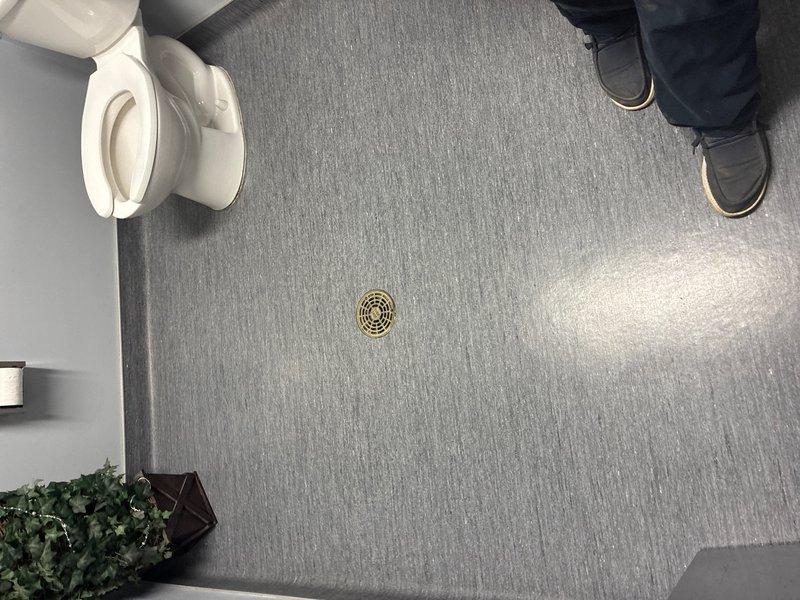 Conducted site assessment of commercial men's bathroom experiencing recurring flooding issues affecting adjacent office space. Inspected existing floor drain system and documented current drain elevation relative to bathroom fixtures and floor level. Provided estimate for drain relocation and lowering to prevent water overflow and protect office areas from future flooding events.