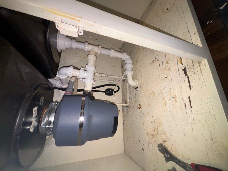 Responded to service call for kitchen sink with no water pressure. Upon inspection, diagnosed low water pressure issue at kitchen faucet. Examined under-sink plumbing configuration including garbage disposal unit, P-trap assembly, and supply line connections. Assessed existing faucet condition and water flow restrictions. Inspected all visible plumbing components beneath sink, including white PVC drainage system and connections to disposal unit. Verified proper operation of shut-off valves and checked for potential blockages or restrictions in supply lines. Documented existing plumbing configuration with cabinet-mounted components and mechanical systems for service records.