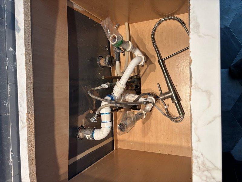 Responded to service call for kitchen sink plumbing requiring installation of new shut-off valves and drain system modifications. Replaced existing cut-off valves with new fixtures, including toilet supply line shut-off that was previously leaking. Updated drain configuration by consolidating multiple drain lines into a single drain assembly beneath the kitchen sink. All plumbing connections were tested for proper operation and verified leak-free. Work completed in finished basement area with full accessibility to plumbing fixtures.