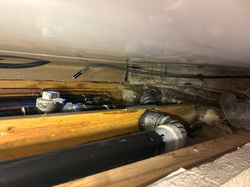 Conducted comprehensive assessment of failed 3" main drain stack serving multiple commercial kitchen sinks. The broken stack was located in the crawl space and exhibited active leaking at critical connection points. Documented existing piping infrastructure including copper supply lines, black ABS drainage piping with visible manufacturer specifications, and associated mechanical systems. Photographed compromised drain stack connections, structural joists, and surrounding plumbing components to provide detailed scope for replacement of the main drainage system serving all kitchen fixtures.