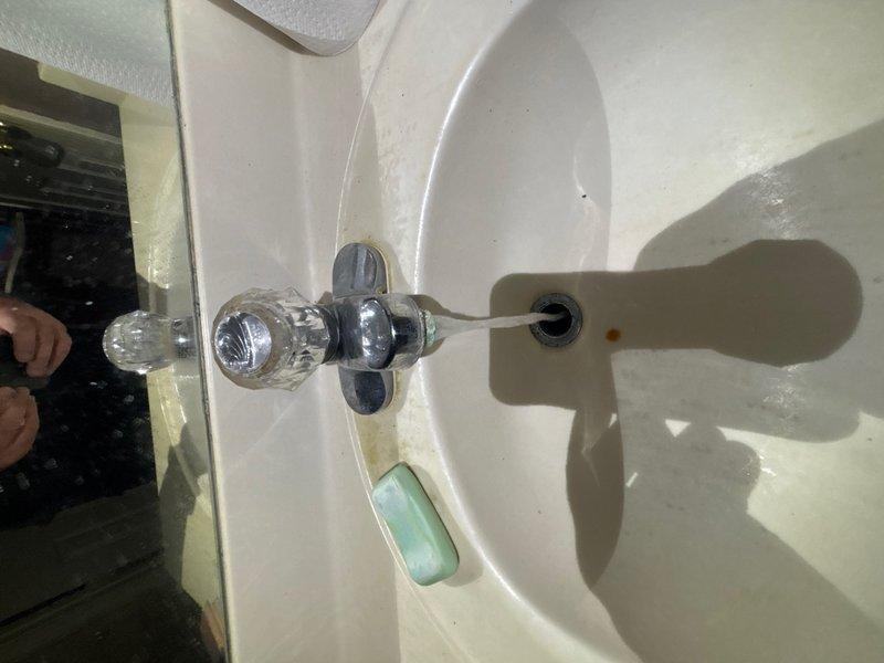 Completed plumbing inspection of second-level bathroom focusing on jacuzzi tub faucet assembly experiencing constant leak. Diagnosed pressure-related leak in faucet mechanism where applying downward pressure on fixture temporarily stops water flow, indicating internal valve seat or cartridge failure. Performed water heater flush as scheduled maintenance. Documented exterior PVC drainage system configuration and bathroom sink plumbing for reference. Recommended faucet cartridge replacement or complete valve assembly repair to resolve leak issue permanently.