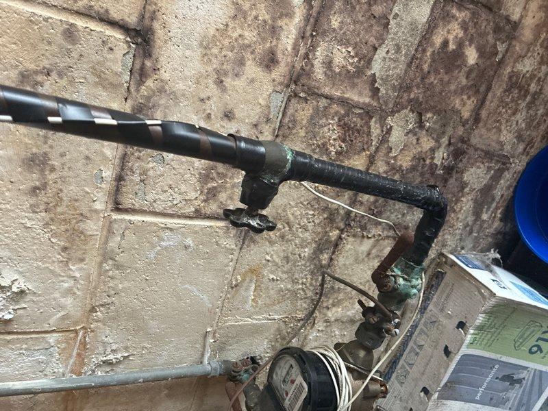 Completed comprehensive plumbing inspection of residential property. Documented aging plumbing infrastructure including deteriorated pipe insulation on main water line, oxidized brass valve assembly showing green patina, and mixed piping materials requiring monitoring. Also photographed exterior HVAC unit positioning and drainage considerations near building foundation.