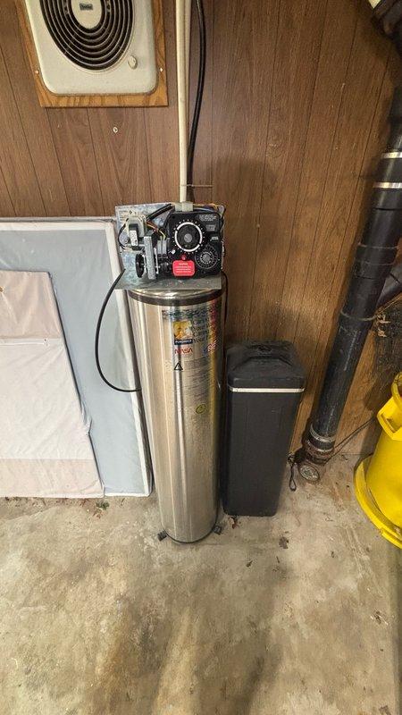 Replaced carbon filter on water softener system located in garage utility area. Serviced cylindrical stainless steel filtration tank with black control head assembly, ensuring proper installation and system functionality. Verified all connections, gauges, and pressure relief components operating correctly upon completion.