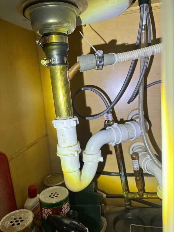 Completed preventive plumbing maintenance inspection on residential property. Inspected and photographed basement plumbing system including water heater, WATTS expansion tank (installed 5/2, over 10 years old), copper supply lines, and drainage components. Examined under-sink plumbing configuration including brass tailpiece, white P-trap with metal hose clamps, and braided stainless steel supply lines. All connections found intact and functional with age-appropriate discoloration on brass components but no active leaks detected.