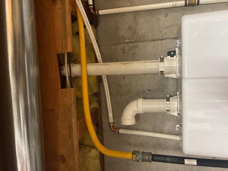 Responded to follow-up service call regarding concerns about tankless water heater installation. Conducted thorough inspection of unit and associated venting system. Documented existing installation with photographs showing PVC vent termination through ceiling with visible rust staining around flange, indicating potential moisture intrusion or condensate issues. Examined mechanical room setup including white tankless unit with PVC exhaust piping, support brackets, and gas line connections. Assessed venting configuration, pipe routing, and proper securing of all components to ensure compliance with manufacturer specifications and local code requirements.