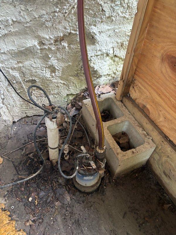 Responded to service call for malfunctioning sump pump system located in backyard crawl space. Upon inspection, found existing pump and discharge piping in severely deteriorated condition with extensive corrosion on copper components, compromised wiring, and significant debris accumulation in the sump pit area. The crawl space environment showed evidence of prolonged moisture exposure with damaged insulation, water-stained surfaces, and organic debris throughout the work area. Documented existing system condition including aged pump motor, corroded plumbing connections, and inadequate drainage setup that contributed to operational failure.