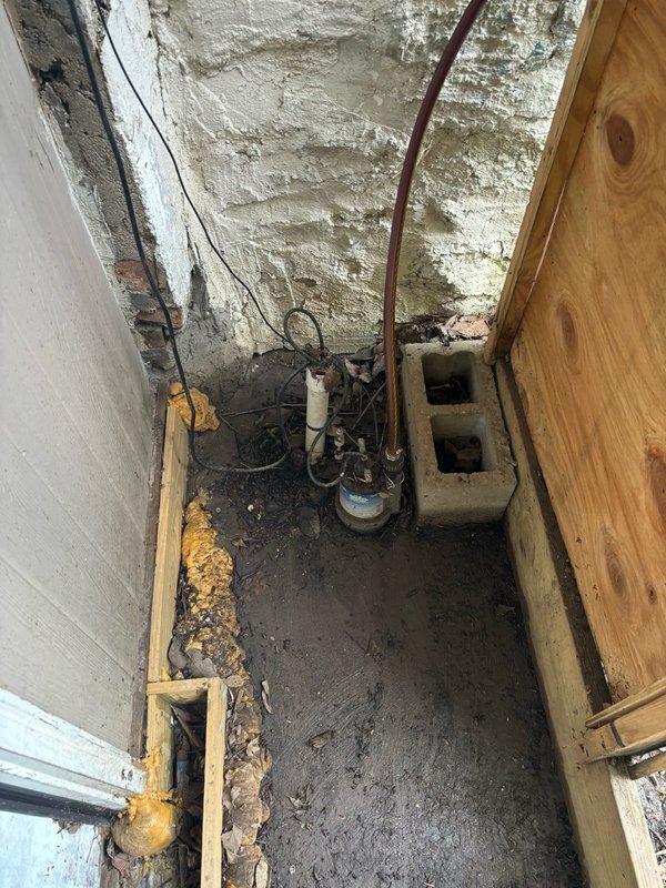 Responded to service call for malfunctioning sump pump system located in backyard crawl space. Upon inspection, found existing pump and discharge piping in severely deteriorated condition with extensive corrosion on copper components, compromised wiring, and significant debris accumulation in the sump pit area. The crawl space environment showed evidence of prolonged moisture exposure with damaged insulation, water-stained surfaces, and organic debris throughout the work area. Documented existing system condition including aged pump motor, corroded plumbing connections, and inadequate drainage setup that contributed to operational failure.