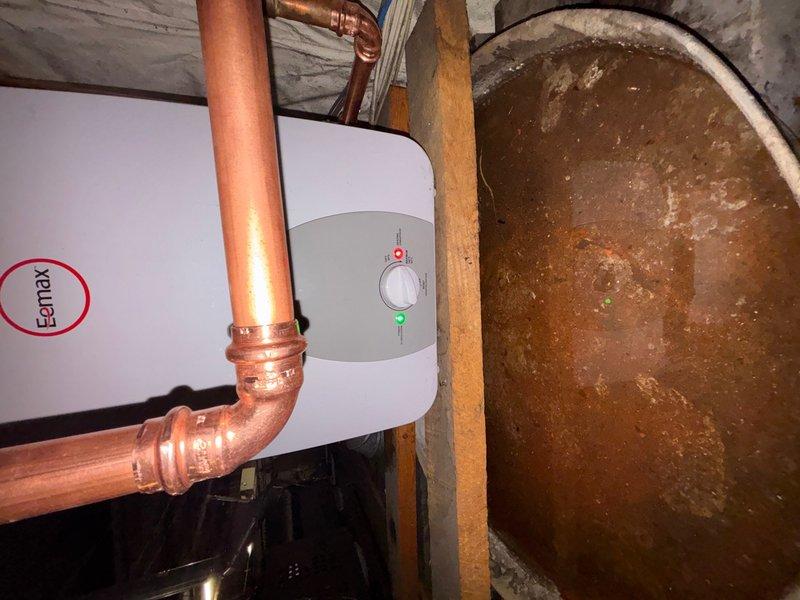 Installed a 6-gallon 120V Eemax electric water heater in commercial basement utility area with thermal expansion tank. Completed copper pipe connections with soldered joints and configured proper inlet/outlet plumbing to integrate unit into existing system. Installation includes proper electrical hookup and drain line routing to floor receptacle.