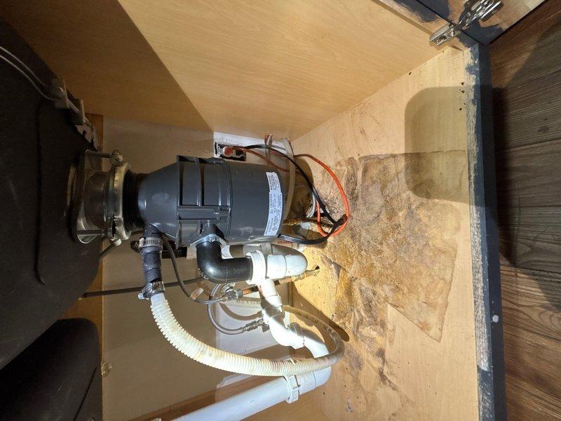 Installed customer-supplied garbage disposal unit under kitchen sink, including complete electrical connections with proper wire terminations and plumbing connections using white PVC drainage pipes and corrugated hoses. Installation includes one-year labor warranty coverage.