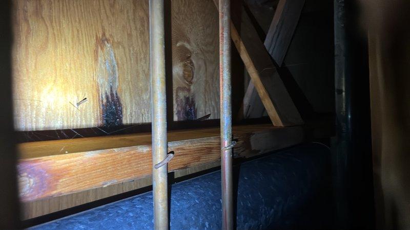 Responded to leak investigation call for water damage in downstairs bathroom ceiling with visible hole. Accessed attic crawl space above affected area and inspected plumbing lines, structural framing, and surrounding insulation. Documented conditions with photos showing galvanized supply lines, HVAC ductwork, floor joists, and insulation between framing members. Performed visual inspection of all visible plumbing connections and pipe runs in vicinity of reported leak location to identify source of water intrusion.