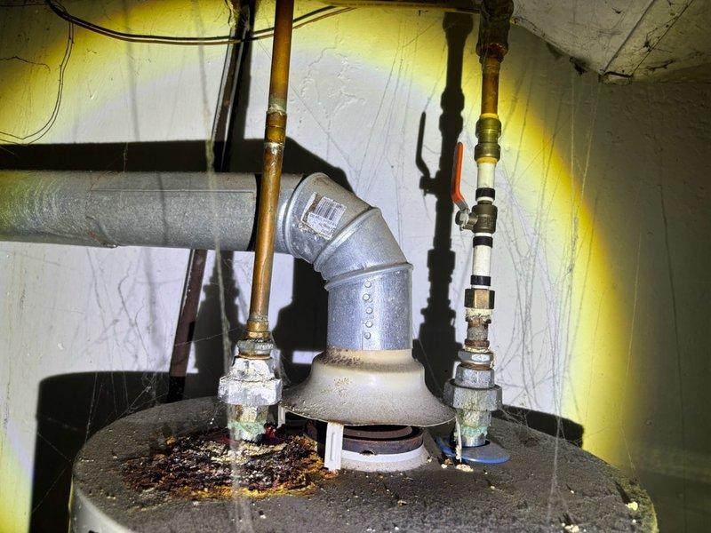 Responded to no hot water complaint in basement. Upon inspection, found significant corrosion and deterioration on galvanized center pipe connection at top of water heater tank, with heavy rust accumulation at base connection point and visible sediment buildup around pipe fittings. Assessed overall condition of aging tanked water heater system, noting corroded fittings and compromised connections affecting hot water delivery. Documented installation condition including copper supply lines, flexible connector, and pressure relief valve configuration for service records.