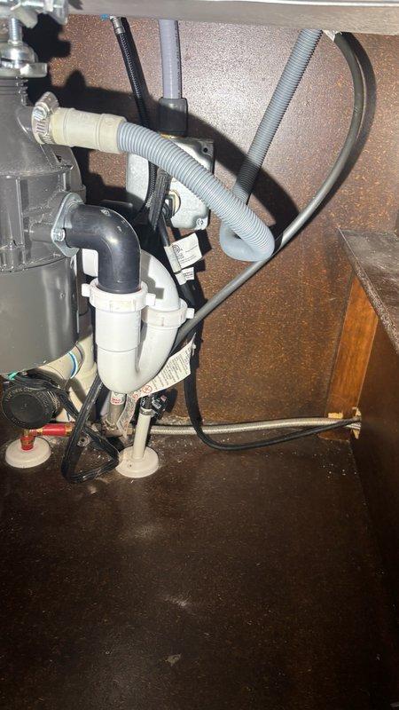 Responded to reported garbage disposal leak in kitchen. Upon inspection, identified active water dripping from disposal unit and surrounding plumbing connections. Examined under-sink plumbing assembly including P-trap configuration, PVC drainage pipes, and disposal mounting hardware. Assessed leak source at disposal unit and associated drain connections. Documented conditions with photographs showing water droplet formation and complete under-sink plumbing layout. Evaluated disposal unit for potential replacement needs and verified all drainage components and electrical connections for proper installation and functionality.