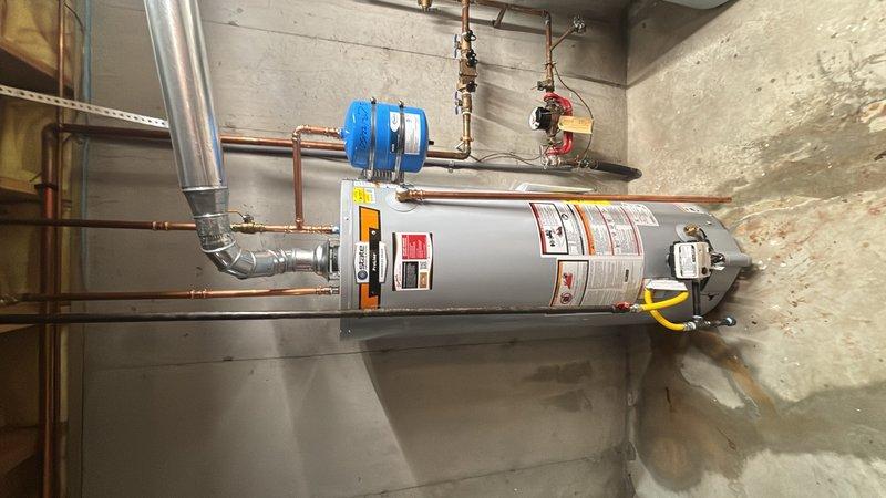 Replaced existing water heater with new 40-gallon gas water heater in basement with walk-out access. Installation included connecting copper supply lines, installing expansion tank with pressure gauge, configuring gas line with flexible connector, and establishing proper venting through existing ductwork. All plumbing connections were secured with appropriate valves and fittings, pressure relief valve installed per code requirements, and system tested for proper operation and leak-free performance.