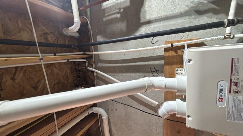 Conducted on-site evaluation of an 11-year-old Noritz tankless water heater system for replacement estimate. Assessed existing installation including gas line connections with flexible corrugated connector, copper supply piping, venting configuration, and mounting location in utility area. Documented current system configuration through photographs showing mechanical room setup with concrete block wall mounting, PVC drainage infrastructure in attic space, and associated plumbing connections. Provided customer with quote for complete removal of existing tankless unit and installation of new tankless water heater system.