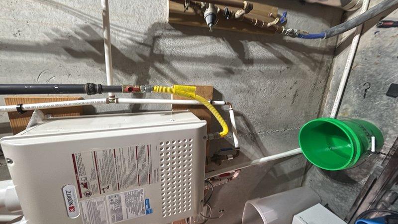 Conducted on-site evaluation of an 11-year-old Noritz tankless water heater system for replacement estimate. Assessed existing installation including gas line connections with flexible corrugated connector, copper supply piping, venting configuration, and mounting location in utility area. Documented current system configuration through photographs showing mechanical room setup with concrete block wall mounting, PVC drainage infrastructure in attic space, and associated plumbing connections. Provided customer with quote for complete removal of existing tankless unit and installation of new tankless water heater system.