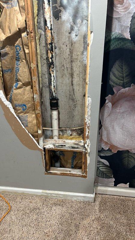 Responded to clogged kitchen drain issue in 40-year-old residential property. Accessed plumbing system through basement crawl space and inspected vertical drain stack. Kitchen sink drainage was completely blocked due to accumulated debris and buildup in the aging black PVC drain line at the Y-junction fitting.

Cleared obstruction using mechanical augering techniques through the cleanout access point. Removed significant grease accumulation and organic matter that had solidified within the pipe over time. Flushed system with water to verify proper flow restoration and confirmed drainage was operating at normal capacity.

Inspected surrounding pipe conditions and noted visible age-related wear on drainage components, including whitish mineral deposits on pipe surfaces. Documented existing moisture damage to adjacent fiberglass insulation and deteriorated wooden structural members around the plumbing chase. Observed advanced decay and dark staining on wall studs indicating long-term wate