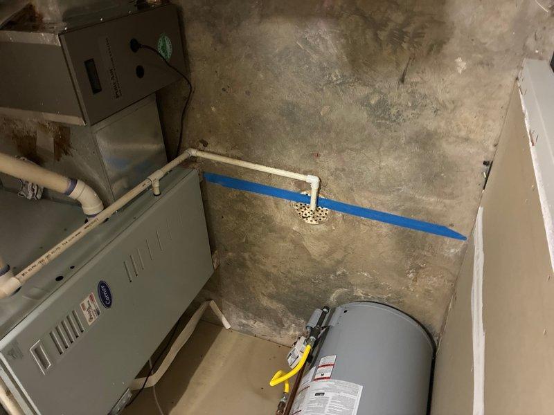 Conducted on-site assessment of commercial building's main sewer drain line to provide estimate for repair or replacement due to identified belly in the line. Inspected interior plumbing cabinet containing vertical PVC drainage system with blue rubber couplings, and evaluated mechanical room housing furnace, water heater, and associated drainage infrastructure including horizontal blue PVC pipe and vertical white PVC drain with floor connection. Documented existing plumbing configuration and conditions to prepare comprehensive bid as part of three-estimate requirement for building's board of directors.