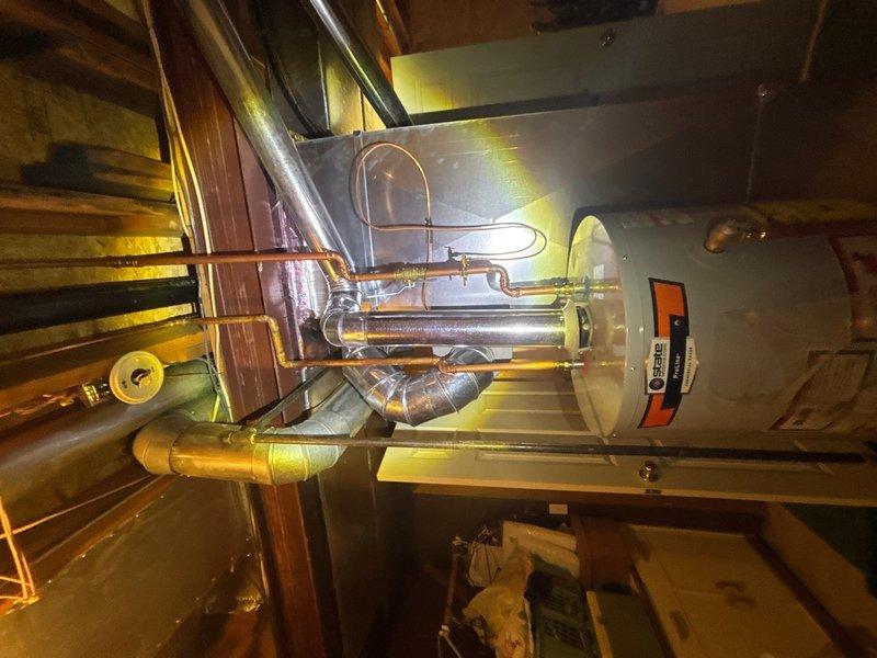 Completed plumbing maintenance inspection of water heater and pressure tank system. Inspected all copper piping connections, brass fittings, pressure relief valve configuration, and pressure gauge at T-fitting junction, confirming proper installation and operation of both the water heater unit and blue pressure tank with associated plumbing components.