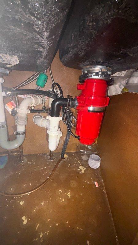 Responded to a clogged kitchen drain in a 20-year-old residential property. Upon arrival, assessed the under-sink plumbing assembly which included a red garbage disposal unit with white PVC trap and drain lines. The sink basin showed significant debris accumulation around the brass drain fitting, indicating blockage in the drainage system.

Performed diagnostic inspection of the disposal unit and connected drain lines to identify the source of the clog. Cleared the obstruction from the kitchen sink drain line, removing accumulated food particles, grease buildup, and debris that had restricted water flow. Tested the garbage disposal for proper operation and verified electrical connections were secure.

Flushed the drain system thoroughly to ensure complete removal of blockage and confirmed proper drainage flow. Inspected all PVC connections, trap assembly, and mounting hardware for leaks or deterioration. Cleaned the sink basin and drain area, removing residual debris. System restored t