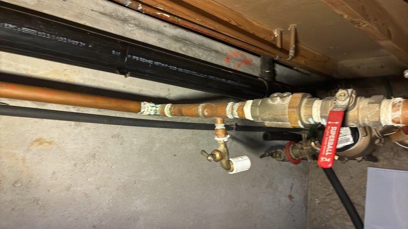Responded to service call for backflow preventer installation estimate. Upon arrival, assessed existing plumbing infrastructure in basement utility area, which included aged copper supply lines with multiple brass fittings, valves, and connection points showing oxidation and wear. Evaluated the current piping configuration running beneath floor joists to determine optimal placement and integration point for new backflow prevention device. Documented existing conditions including insulated copper lines, shutoff valves, and parallel black piping systems. Photographed the installation area showing the horizontal pipe runs, connection points, and available access for future installation work. Provided comprehensive estimate for backflow preventer installation including required materials, labor, and necessary modifications to integrate device into existing water supply system while maintaining proper clearances and accessibility for testing and maintenance requirements per local plumbing c