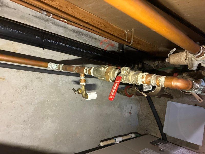 Responded to service call for backflow preventer installation estimate. Upon arrival, assessed existing plumbing infrastructure in basement utility area, which included aged copper supply lines with multiple brass fittings, valves, and connection points showing oxidation and wear. Evaluated the current piping configuration running beneath floor joists to determine optimal placement and integration point for new backflow prevention device. Documented existing conditions including insulated copper lines, shutoff valves, and parallel black piping systems. Photographed the installation area showing the horizontal pipe runs, connection points, and available access for future installation work. Provided comprehensive estimate for backflow preventer installation including required materials, labor, and necessary modifications to integrate device into existing water supply system while maintaining proper clearances and accessibility for testing and maintenance requirements per local plumbing c