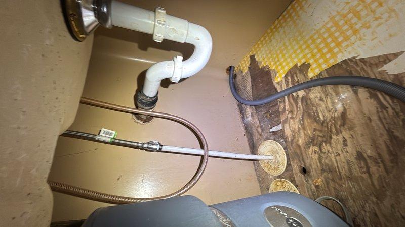 Responded to kitchen water leak complaint with water appearing on floor during washer operation and slow drainage on garbage disposal. Upon inspection, identified water damage to cabinet floor beneath sink with significant staining and deterioration of wooden surfaces. Examined P-trap assembly, water supply lines, and drainage connections for source of leak. Investigated plumbing connections associated with washing machine discharge and garbage disposal drain line. Documented existing water damage and compromised cabinet materials resulting from moisture exposure. Addressed drainage issue affecting garbage disposal operation and traced potential leak sources in under-sink plumbing system.