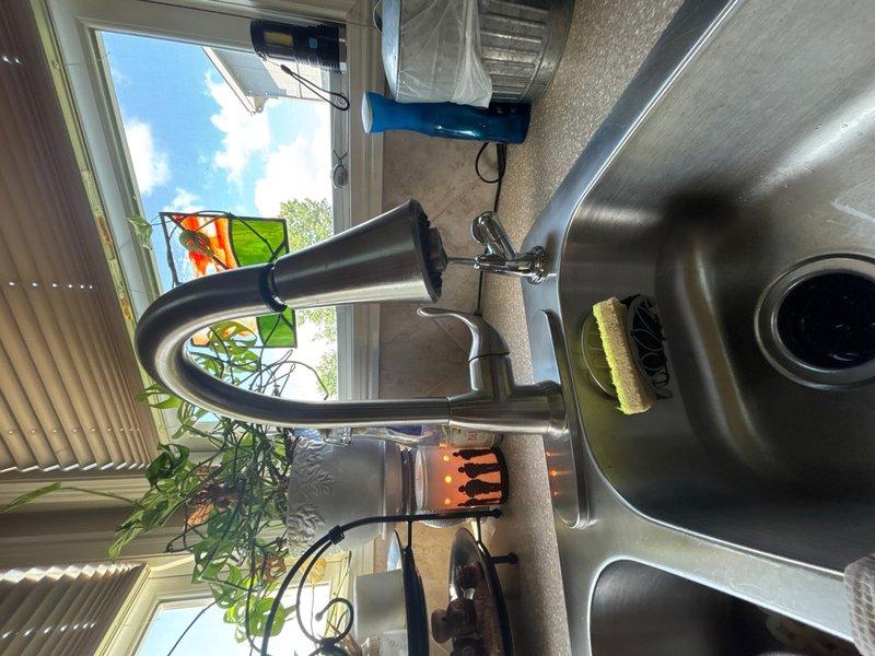 Successfully installed new kitchen faucet with modern curved spout design over dual-basin stainless steel sink. Verified proper water supply connections, tested flow and drainage through existing P-trap plumbing assembly, and confirmed no leaks at all connection points.