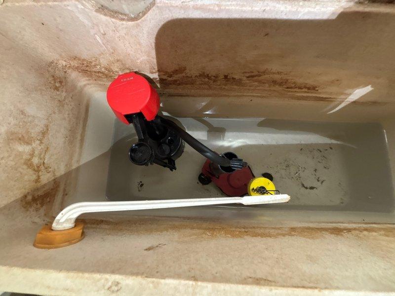 Responded to reported toilet leak in basement bathroom. Upon inspection, found extensive water staining on ceramic tile flooring surrounding toilet base, indicating chronic leakage. Inspected toilet tank interior and identified deteriorated flush valve flapper as primary source of leak. Tank showed significant mineral deposits and rust staining on interior surfaces, confirming prolonged water seepage. Replaced worn red rubber flapper assembly and inspected water supply line connection for integrity. Tested flush mechanism multiple times to ensure proper seal and verified no active leaking from tank or base connection. Documented pre-repair conditions showing floor discoloration and tank component deterioration.