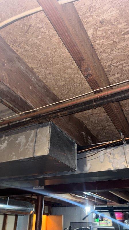 Responded to complaint of loud, intermittent bumping noises in water pipes occurring throughout the day, even when water was not in use. Inspected plumbing system in basement/crawl space of 1970s-era home where previous service call had not identified the cause. Diagnosed water hammer condition caused by inadequate air chambers and possible loose pipe mounting. Examined exposed copper and black piping runs, checked shut-off valves and mounting brackets for proper securing. Installed water hammer arrestor at strategic location to absorb hydraulic shock and prevent pressure spikes in the system. Secured loose pipe hangers and added additional support brackets where needed to minimize pipe movement and vibration transmission through structural framing.