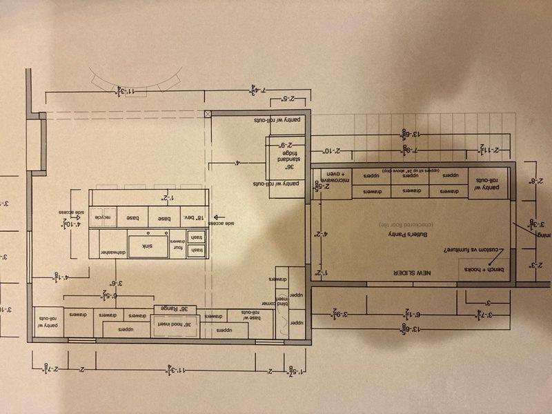Conducted site visit to assess plumbing requirements for kitchen relocation project. Reviewed architectural floor plans showing new kitchen layout including butler's pantry and revised room configurations. Inspected existing plumbing infrastructure in basement/crawlspace area, documenting current pipe routing through floor joists including white PVC drain lines and copper supply lines. Evaluated structural constraints and existing pipe penetrations to develop estimate for new water supply piping and drain installation required to accommodate relocated kitchen fixtures and appliances.