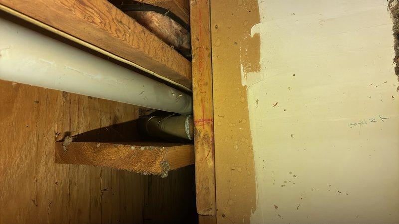 Conducted site visit to assess plumbing requirements for kitchen relocation project. Reviewed architectural floor plans showing new kitchen layout including butler's pantry and revised room configurations. Inspected existing plumbing infrastructure in basement/crawlspace area, documenting current pipe routing through floor joists including white PVC drain lines and copper supply lines. Evaluated structural constraints and existing pipe penetrations to develop estimate for new water supply piping and drain installation required to accommodate relocated kitchen fixtures and appliances.