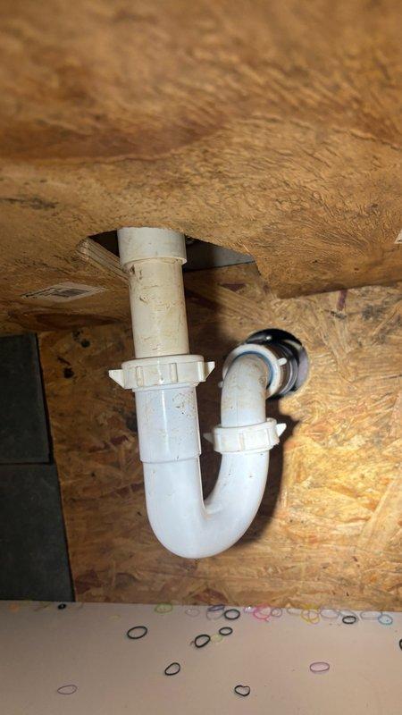 Responded to service call for reported water leak under bathroom sink and drainage issues. Upon inspection, examined white PVC P-trap assembly and drain connections for signs of leakage and obstruction. Assessed plumbing fixture mounting and verified proper installation of trap components and threaded connections. Inspected accessible crawl space and attic areas to evaluate potential water damage, checking ductwork, insulation, and structural framing for moisture intrusion or corrosion. Documented existing conditions including rust streaking on metal ductwork and fiberglass insulation status. Provided professional assessment and second opinion on plumbing system condition to assist with repair decision-making.