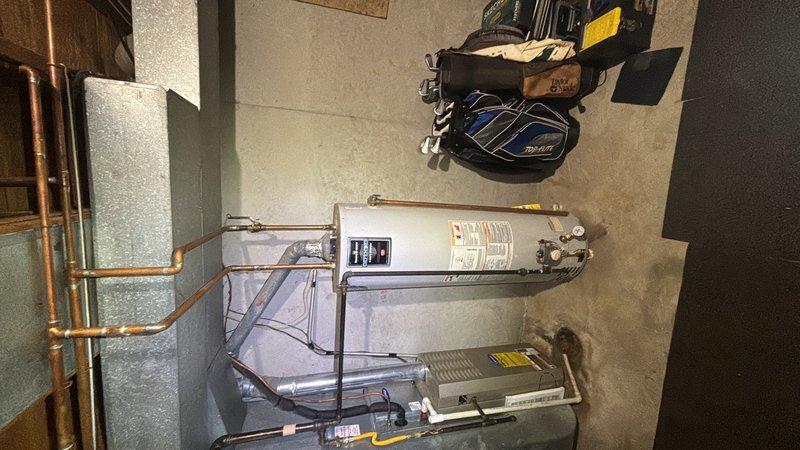 Responded to basement water heater leak on unit approximately 20 years old. Performed on-site assessment of 50-gallon gas water heater showing signs of age-related deterioration and active leaking while still maintaining hot water production. Inspected all plumbing connections, pressure relief valve, gas lines, and copper piping configuration. Documented existing installation including HVAC integration, pressure gauge readings, and overall system condition. Provided estimate for water heater replacement with new 50-gallon gas unit including proper venting, gas line connections, and code-compliant installation.