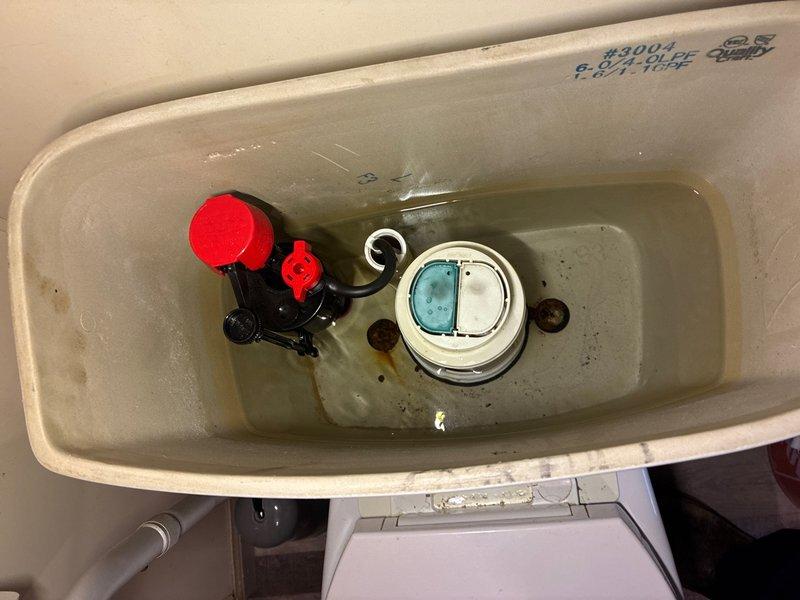Responded to service call for a toilet that was constantly running. Upon inspection, removed tank lid and identified faulty flapper seal on the flush valve assembly causing continuous water flow from tank to bowl. Observed discolored water with sediment accumulation in tank and mineral deposits on interior surfaces. Replaced defective flapper mechanism and adjusted fill valve assembly with red float cap to ensure proper water level and shutoff function. Tested flush cycle multiple times to verify complete seal and proper refill operation. Photographed internal tank components showing dual-flush button assembly, fill valve, and flush valve configuration for service records. System now functioning properly with no continuous running or water waste.
