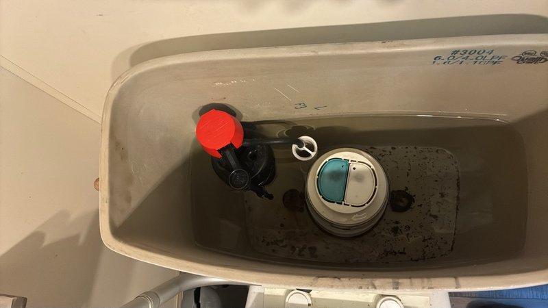 Responded to service call for a toilet that was constantly running. Upon inspection, removed tank lid and identified faulty flapper seal on the flush valve assembly causing continuous water flow from tank to bowl. Observed discolored water with sediment accumulation in tank and mineral deposits on interior surfaces. Replaced defective flapper mechanism and adjusted fill valve assembly with red float cap to ensure proper water level and shutoff function. Tested flush cycle multiple times to verify complete seal and proper refill operation. Photographed internal tank components showing dual-flush button assembly, fill valve, and flush valve configuration for service records. System now functioning properly with no continuous running or water waste.