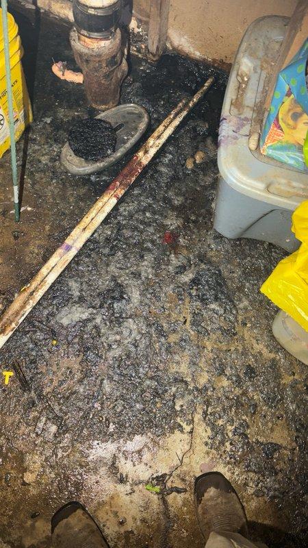 Responded to a backed up main drain in the basement. Upon arrival, found significant sewage backup with black residue covering the utility room floor. Cleared the main drain line obstruction and restored proper drainage flow. Inspected the vertical PVC drain and waste piping system running through the wall cavity to verify proper function and ensure no additional blockages in the secondary lines. Cleanup of affected area completed following successful drain clearing.