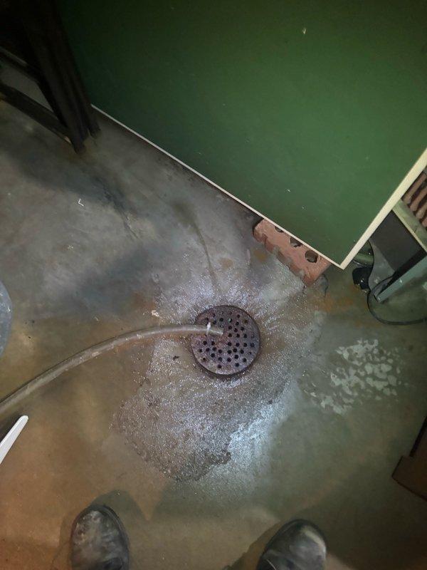 Responded to water heater leak in basement of mid-century modern home. Upon arrival, found active water accumulation on concrete floor surrounding floor drain, with visible pooling and moisture spread across basement surface. Inspected water heater unit and identified source of leak. Documented existing water damage and staining patterns on concrete floor indicating ongoing or previous water infiltration. Assessed drainage system functionality and confirmed floor drain was operational. Completed diagnostic evaluation of water heater condition and leak severity, captured photographic documentation of affected area and water damage extent for service records.