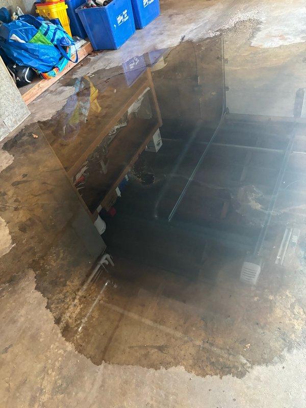 Responded to a backed up floor drain in the garage. Upon arrival, found significant standing water in a recessed pit area containing HVAC equipment, with water levels high enough to submerge most of the unit. Assessed the drainage system which included aging plumbing infrastructure with corroded valve assemblies and deteriorated piping. Cleared the clogged floor drain to restore proper drainage function and prevent further water accumulation around the mechanical equipment. The blockage was successfully removed, allowing standing water to drain and restoring normal floor drain operation.