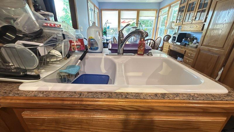 Completed estimate for replacement of existing double-basin kitchen sink with customer-supplied fixture. Current sink is functional with standard chrome faucet and blue garbage disposal unit installed. Assessed existing plumbing configuration including PVC drainage system and disposal connections to ensure compatibility with new fixture installation.