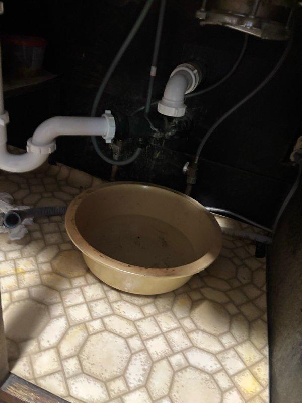 Responded to reported kitchen sink clog and performed diagnostic assessment of drainage system. Upon inspection, accessed plumbing infrastructure in basement utility area beneath kitchen to evaluate drainage lines and identify blockage source. Documented existing plumbing configuration including PVC drainage piping, copper supply lines, and mechanical connections. Prepared work area with catch basin positioned under drainage system to contain water during diagnostic procedures and potential repair work.